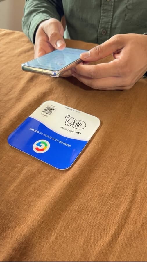 A Google review card on a shop counter, tapped with a phone (5)